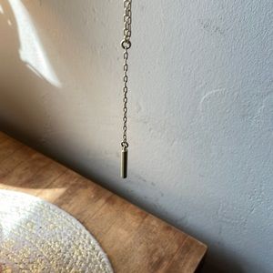 Long, gold necklace with cylinder gold color pennant.